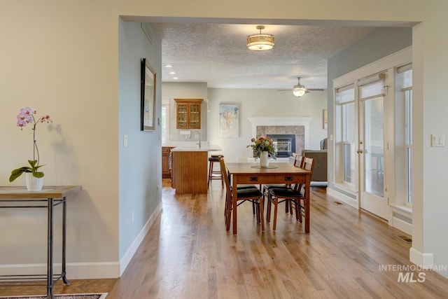 16089 N Basin Way, Boise, ID 83714 - dining area featuring ceiling fan, a textured ceiling, light wood-style flooring, a tiled fireplace, and baseboards