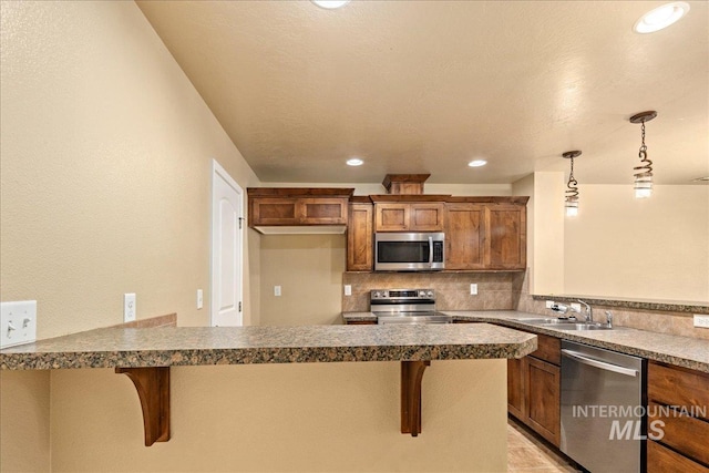 kitchen with brown cabinets, a sink, tasteful backsplash, appliances with stainless steel finishes, and a peninsula