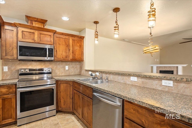 kitchen with brown cabinets, a sink, stainless steel appliances, decorative backsplash, and a tile fireplace