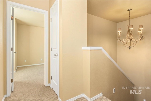 hallway featuring a notable chandelier, an upstairs landing, baseboards, and carpet floors