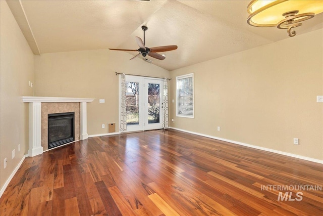 unfurnished living room with wood finished floors, baseboards, ceiling fan, vaulted ceiling, and a tiled fireplace