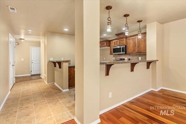 kitchen featuring brown cabinetry, visible vents, baseboards, a breakfast bar, and stainless steel microwave