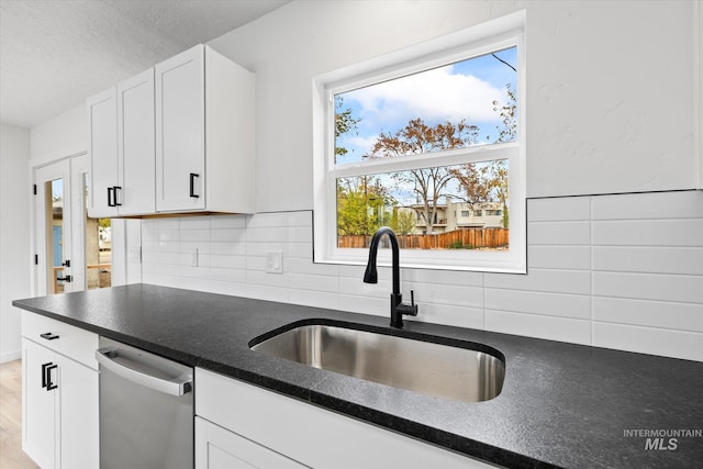 kitchen featuring stainless steel dishwasher, sink, white cabinetry, and backsplash