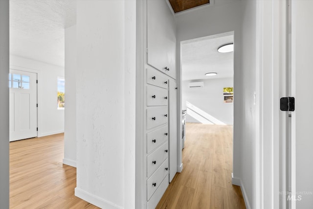 hall with a wall mounted air conditioner, light hardwood / wood-style flooring, and a textured ceiling