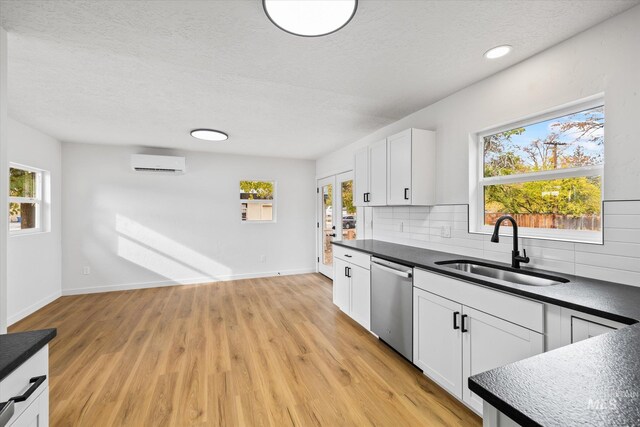 kitchen featuring white cabinets, a wall mounted AC, stainless steel dishwasher, light hardwood / wood-style flooring, and sink