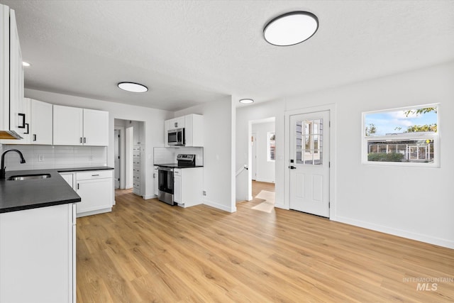 kitchen featuring white cabinets, tasteful backsplash, appliances with stainless steel finishes, light hardwood / wood-style flooring, and sink