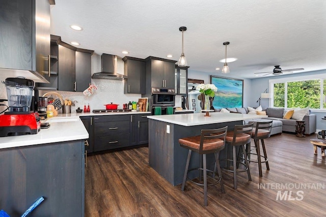 kitchen featuring sink, wall chimney range hood, dark hardwood / wood-style flooring, decorative light fixtures, and a kitchen island