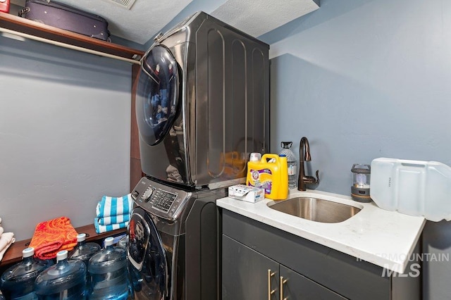 clothes washing area with a textured ceiling, sink, cabinets, and stacked washer / dryer