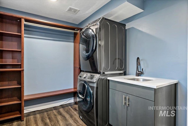 laundry room featuring sink, cabinets, dark wood-type flooring, a textured ceiling, and stacked washer / drying machine