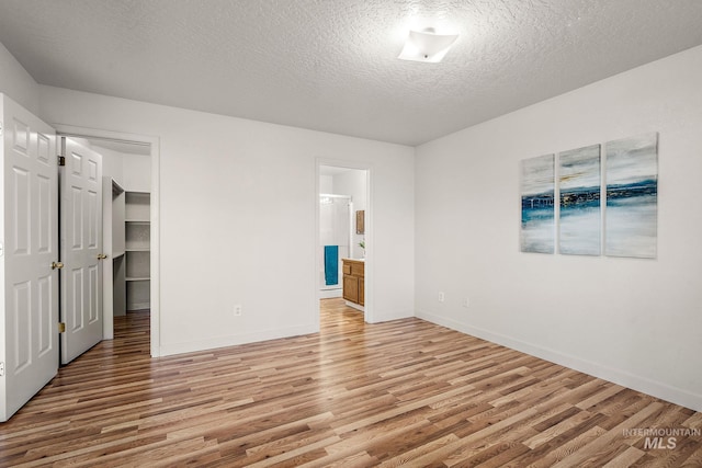 unfurnished bedroom with connected bathroom, light hardwood / wood-style floors, a textured ceiling, a walk in closet, and a closet