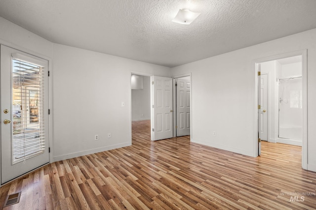 unfurnished bedroom with access to outside, ensuite bath, light hardwood / wood-style flooring, and a textured ceiling