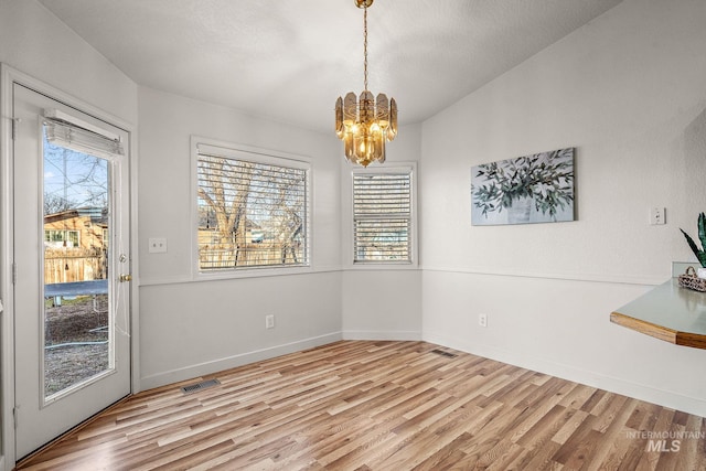 unfurnished dining area featuring light hardwood / wood-style floors, an inviting chandelier, and plenty of natural light