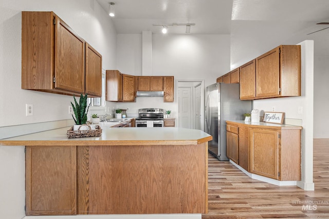 kitchen featuring kitchen peninsula, stainless steel appliances, sink, light hardwood / wood-style flooring, and a high ceiling