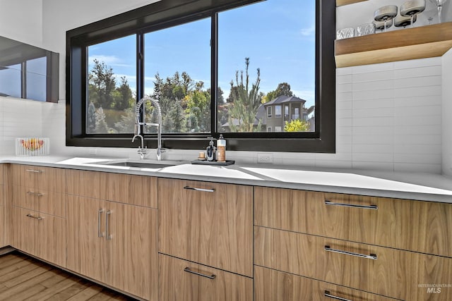 kitchen with a sink, light wood finished floors, tasteful backsplash, and light countertops