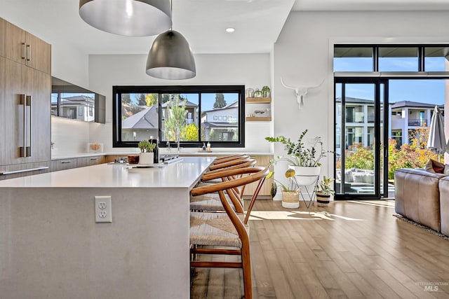 kitchen with wood finished floors, a kitchen island, light countertops, a kitchen breakfast bar, and modern cabinets