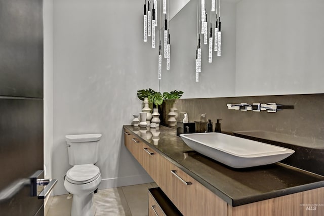 bathroom with tile patterned floors, toilet, decorative backsplash, baseboards, and vanity