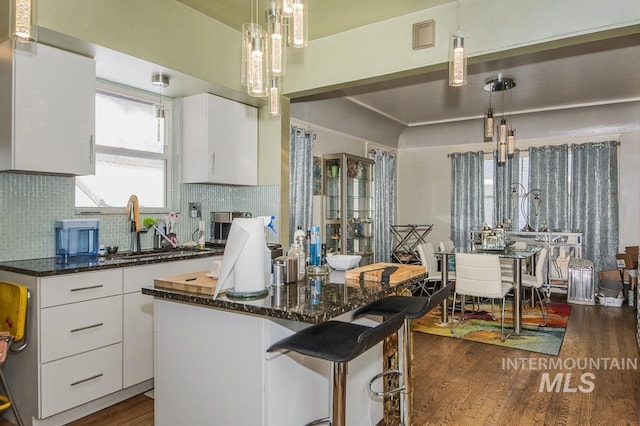 kitchen with a kitchen island, sink, white cabinets, dark stone counters, and hanging light fixtures