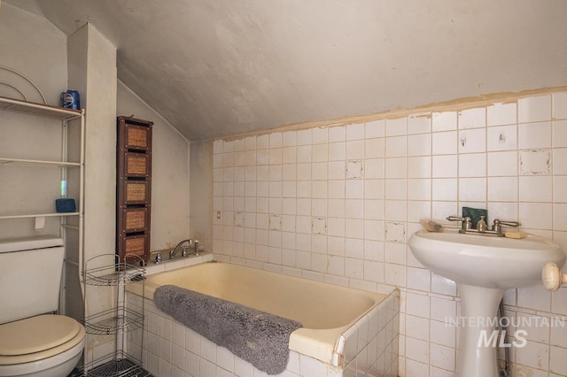 bathroom featuring lofted ceiling, tiled tub, tile walls, and toilet