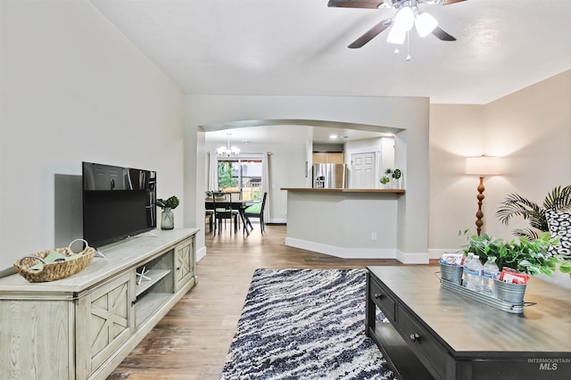 living room with ceiling fan with notable chandelier and light hardwood / wood-style floors