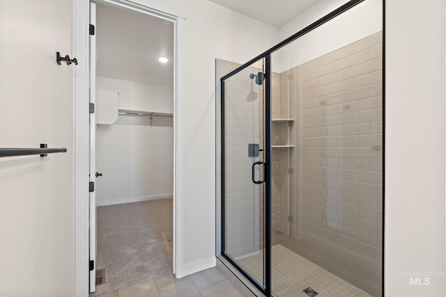 bathroom featuring a walk in closet, a shower stall, baseboards, and tile patterned flooring