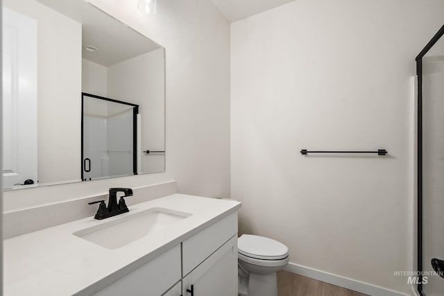 bathroom featuring vanity, wood finished floors, baseboards, a shower stall, and toilet