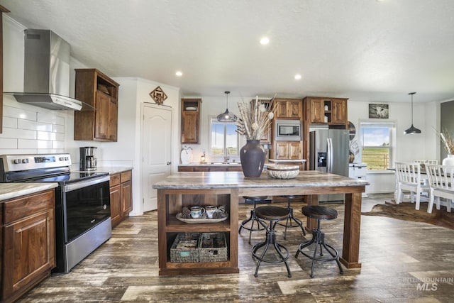 kitchen featuring hanging light fixtures, wall chimney exhaust hood, appliances with stainless steel finishes, and open shelves