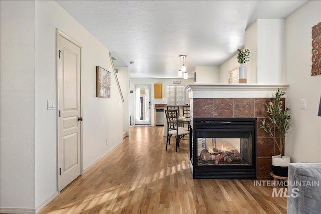 living room featuring a multi sided fireplace, baseboards, and wood finished floors