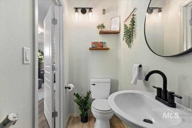 bathroom featuring wood finished floors, a sink, baseboards, toilet, and a textured wall
