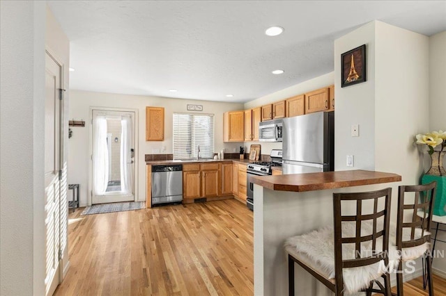 kitchen featuring a kitchen breakfast bar, dark countertops, a sink, light wood finished floors, and stainless steel appliances