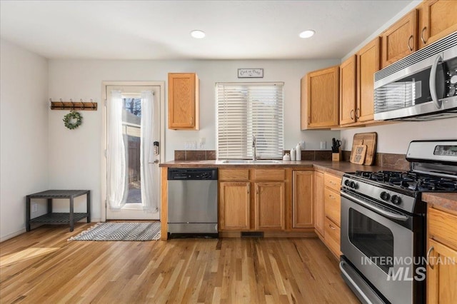 kitchen featuring light wood-type flooring, a sink, dark countertops, and stainless steel appliances