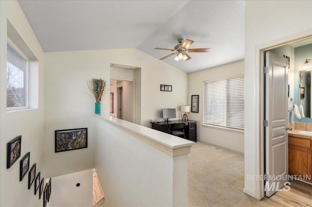 hallway with an upstairs landing, plenty of natural light, lofted ceiling, and light carpet