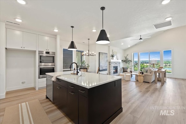 kitchen featuring lofted ceiling, white cabinets, ceiling fan with notable chandelier, hanging light fixtures, and stainless steel appliances