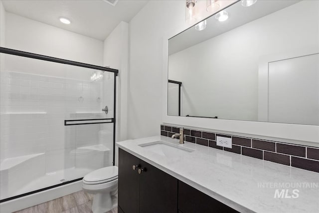 bathroom with backsplash, vanity, a shower with shower door, and toilet