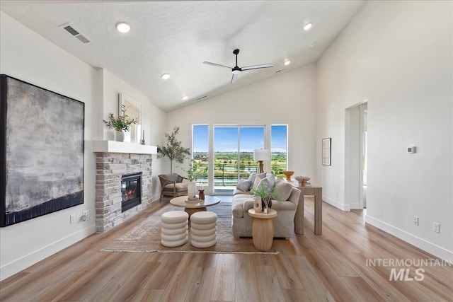 living room with ceiling fan, light hardwood / wood-style floors, a stone fireplace, and high vaulted ceiling