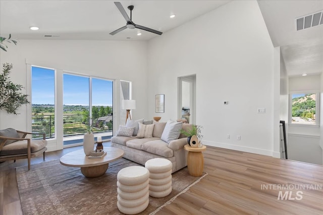 living room with a towering ceiling, light hardwood / wood-style flooring, ceiling fan, and a healthy amount of sunlight