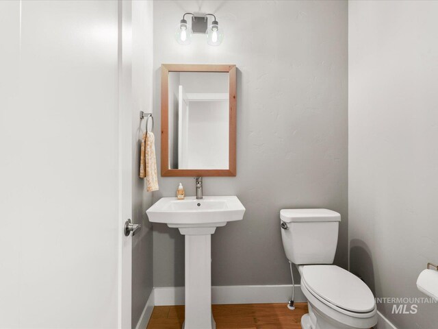 bathroom featuring toilet, wood finished floors, baseboards, and a sink
