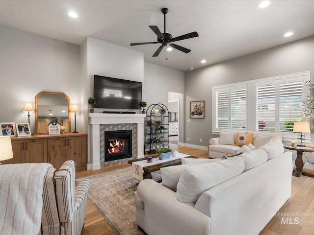 living room featuring ceiling fan, light wood finished floors, recessed lighting, a tiled fireplace, and baseboards