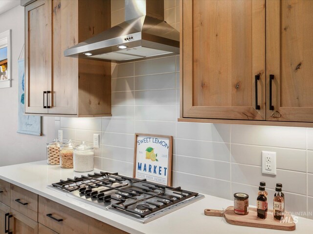 kitchen with wall chimney exhaust hood, stainless steel gas cooktop, tasteful backsplash, and light countertops
