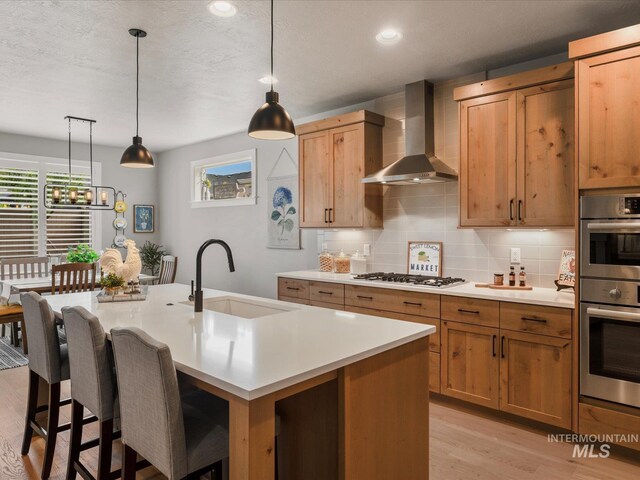 kitchen with wall chimney exhaust hood, a sink, healthy amount of natural light, light wood-style floors, and recessed lighting