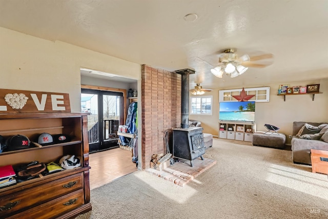 carpeted living room with a wood stove and ceiling fan