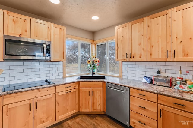 kitchen with decorative backsplash, light stone counters, stainless steel appliances, sink, and light hardwood / wood-style flooring