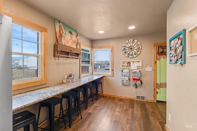 kitchen with a kitchen breakfast bar, light stone countertops, and dark hardwood / wood-style flooring