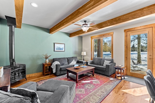 living room with a wealth of natural light, beamed ceiling, wood finished floors, and a wood stove