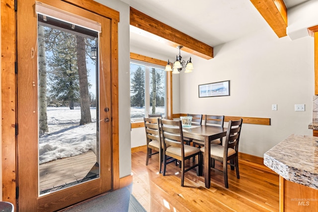 dining area with baseboards, light wood finished floors, beamed ceiling, and an inviting chandelier