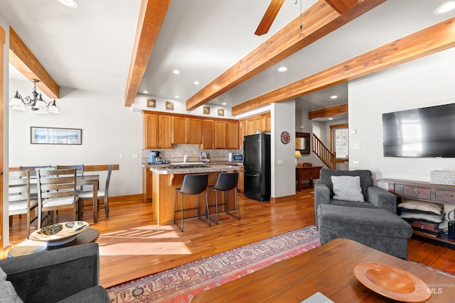 living area with light wood-style floors, stairway, and beamed ceiling