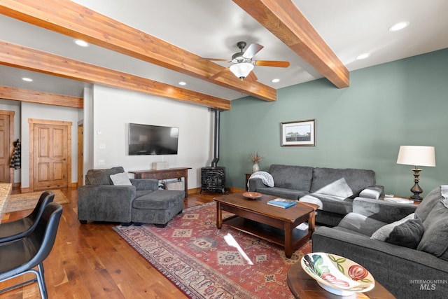 living area featuring recessed lighting, a wood stove, beam ceiling, and wood finished floors