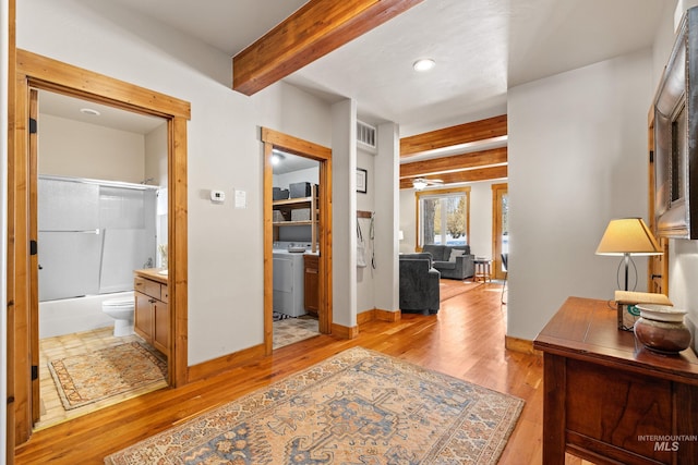 corridor featuring light wood-style flooring, washer and clothes dryer, visible vents, baseboards, and beamed ceiling