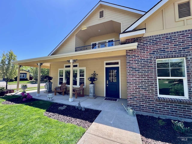 entrance to property featuring a lawn, a porch, brick siding, and a balcony