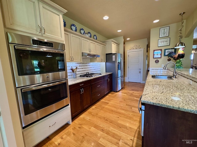 kitchen with under cabinet range hood, tasteful backsplash, a sink, light wood-style flooring, and stainless steel appliances