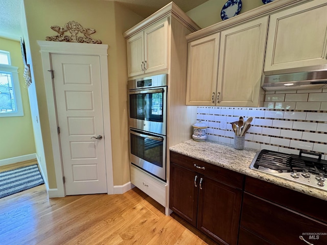 kitchen with light wood finished floors, appliances with stainless steel finishes, backsplash, and light stone countertops
